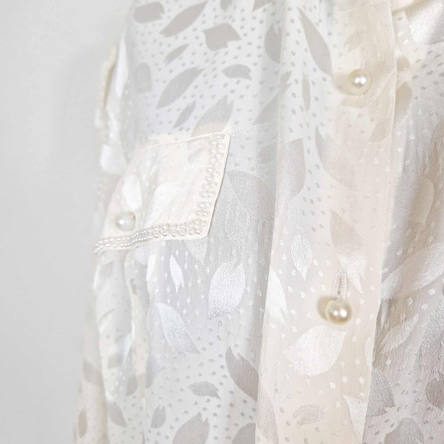 Einzigartige und nachhaltige Vintage Bluse in eierschale mit Perlen. Unique and sustainable vintage blouse in off-white with pearls. Close-up.