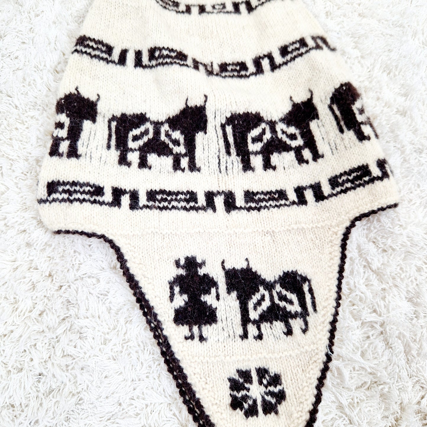 Einzigartige und nachhaltige Vintage Mütze in eierschale-dunkelbraun mit earflap und Kühen. Unique and sustainable vintage hat in offwhite-dark brown with earflap and cows. Close-up.