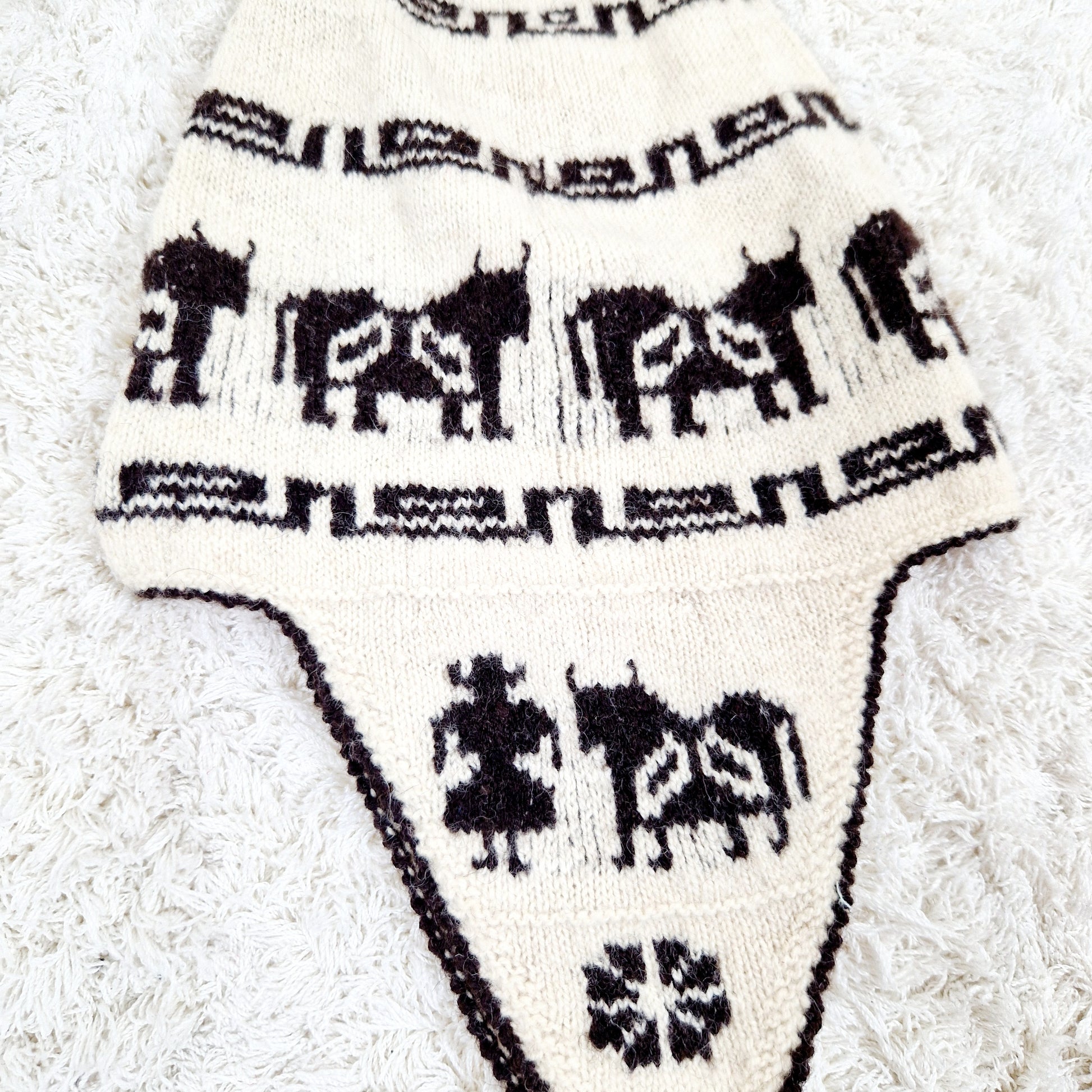 Einzigartige und nachhaltige Vintage Mütze in eierschale-dunkelbraun mit earflap und Kühen. Unique and sustainable vintage hat in offwhite-dark brown with earflap and cows. Close-up.