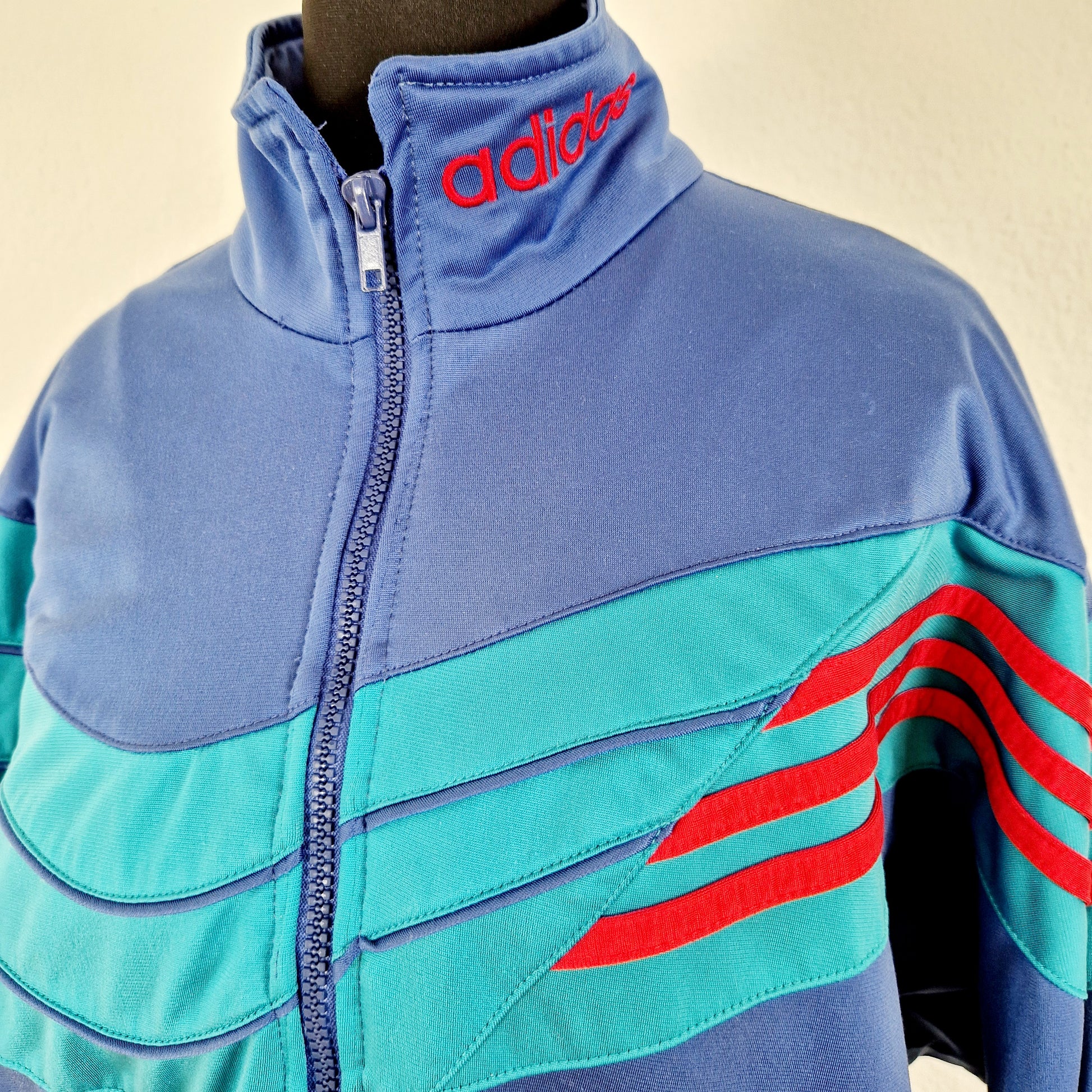 Einzigartige und nachhaltige Vintage Trainerjacke in blau-grün-rot von Adidas. Unique and sustainable vintage track jacket in blue-green-red from Adidas. Close-up.