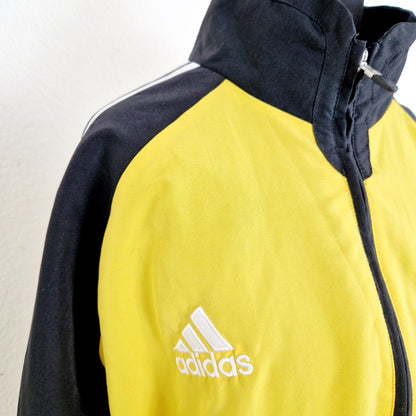Einzigartige und nachhaltige Vintage Trainerjacke von Adidas in gelb-schwarz. Unique and sustainable vintage track jacket from Adidas in yellow-black. Close-up.